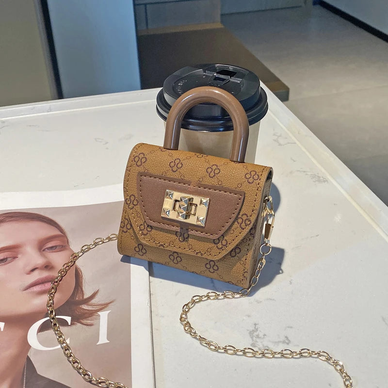 Bolso cruz floral texturizado en tono canela con correa de cadena dorada sobre una superficie blanca.