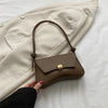 A brown leather crossbody bag is being held against a light beige blazer.