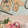 Portefeuille en PVC rose de luxe avec chaîne dorée et porte-clés, attaché à un sac matelassé vert clair.