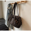 A leopard print canvas tote bag with an adjustable shoulder strap hanging on a wooden rack.