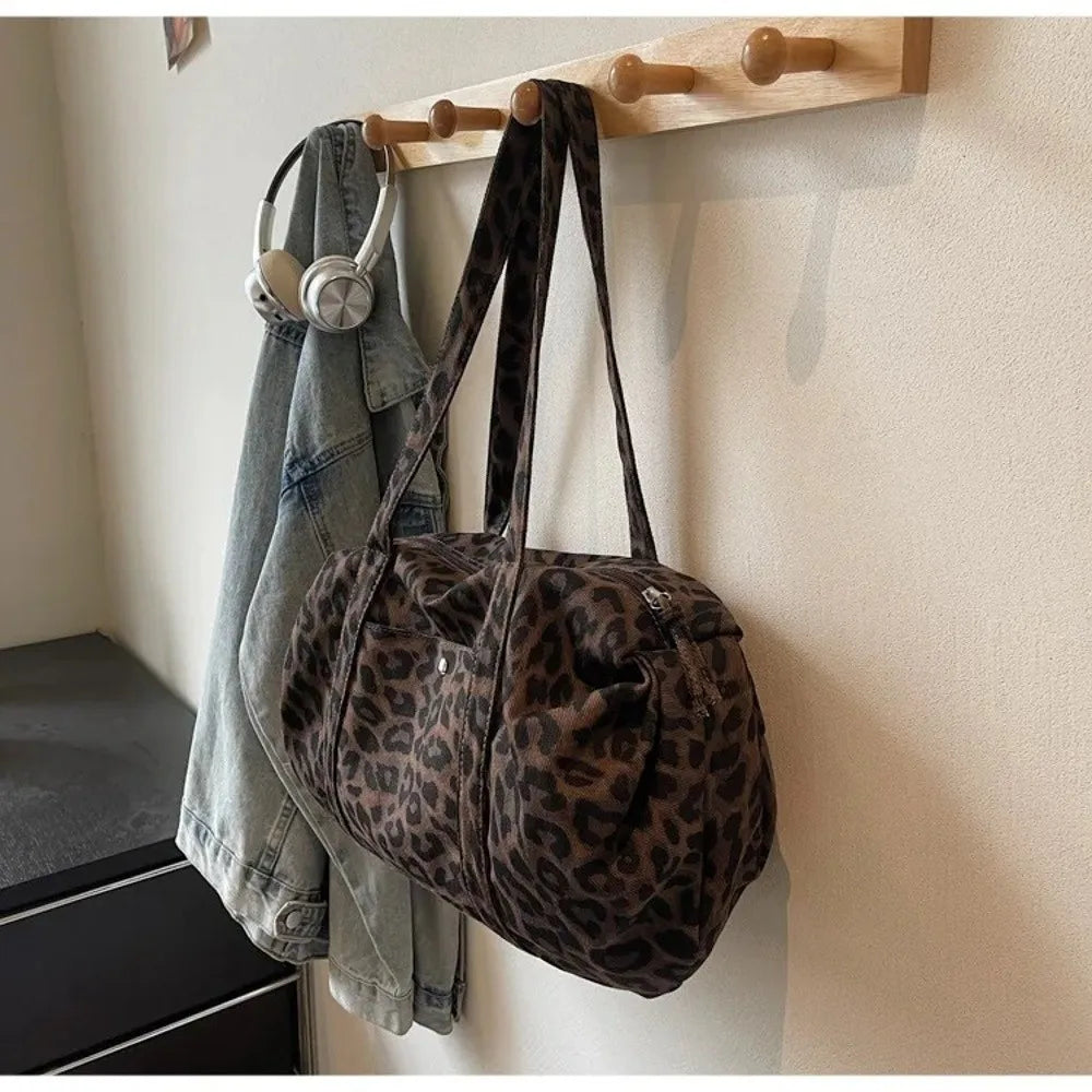 A leopard print canvas tote bag with an adjustable shoulder strap hanging on a wooden rack.