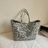A black and white leopard print canvas tote bag with handles resting on a white surface.