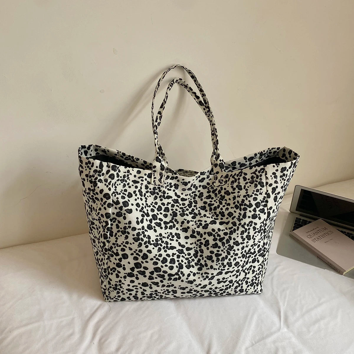 A black and white leopard print canvas tote bag with handles resting on a white surface.