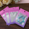 Three resealable gradient storage bags in pink and purple holding jewelry or supplies on a wooden surface.