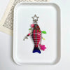 A colorful simulation fish keychain with a star charm resting on a white square dish.