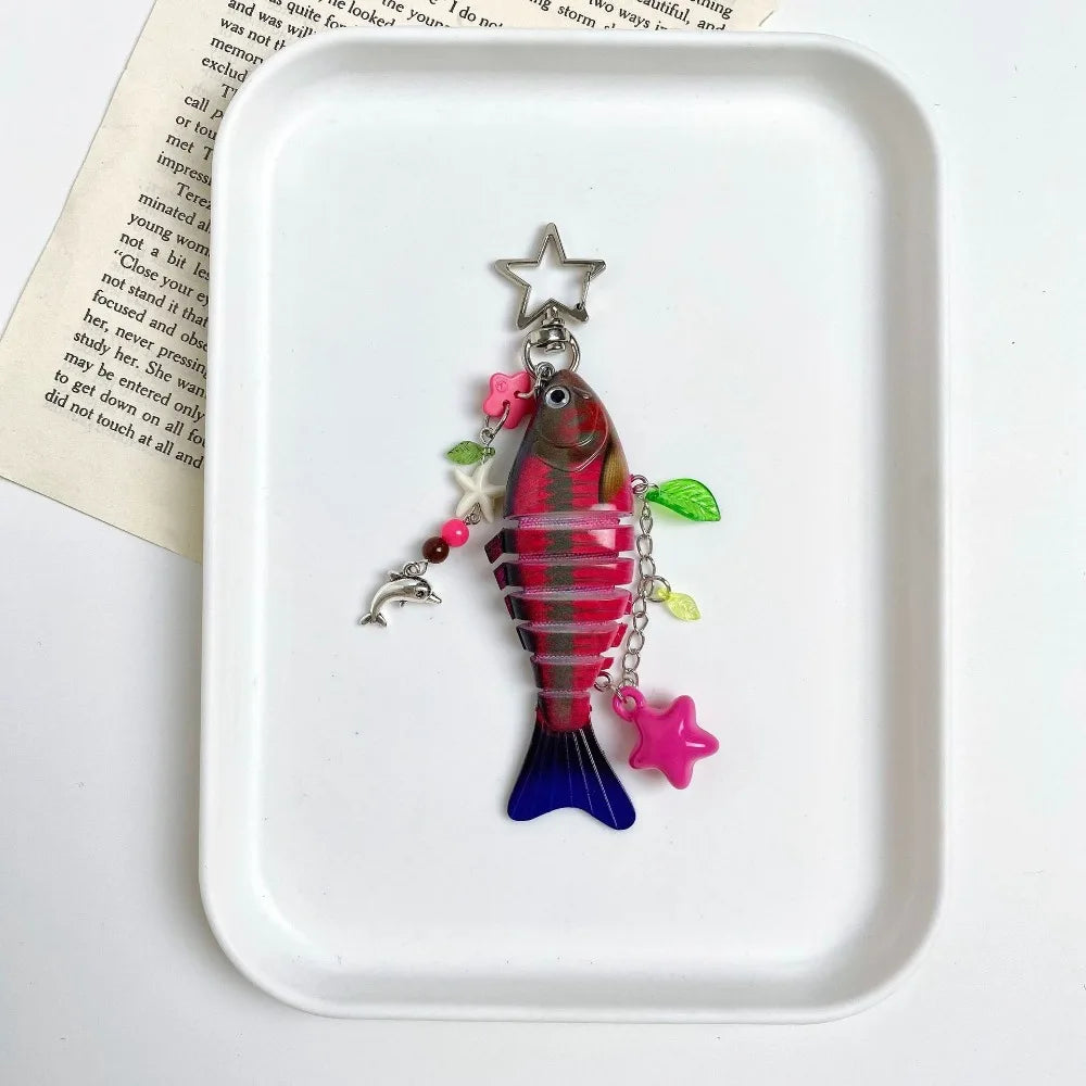 A colorful simulation fish keychain with a star charm resting on a white square dish.