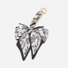 A black and white floral patterned bow bag chain strap extension with a gold-colored ring.
