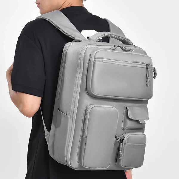 Une personne porte un grand sac de voyage gris avec plusieurs compartiments.