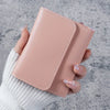 A hand holds a light pink leather card wallet with stitched edges against a gray background.