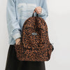 A brown leopard print laptop backpack worn by a person in a light blue sweatshirt.