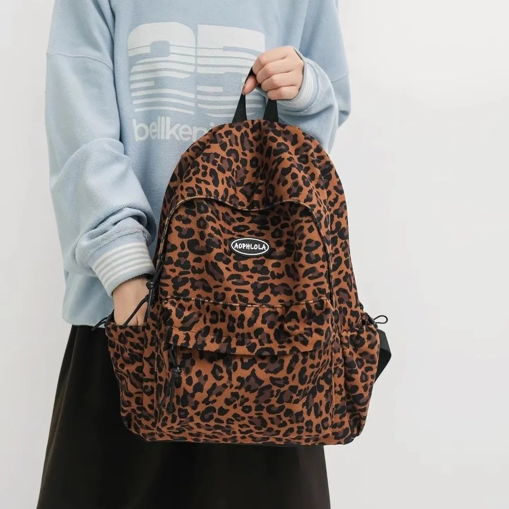 A brown leopard print laptop backpack worn by a person in a light blue sweatshirt.