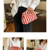 A woman holds a red and white striped crochet handbag against a white shirt.