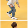 A young boy wearing a gray cartoon animal plush backpack while standing against a yellow background.
