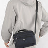 A man wearing a light gray jacket is holding a navy blue compact waterproof crossbody messenger bag.