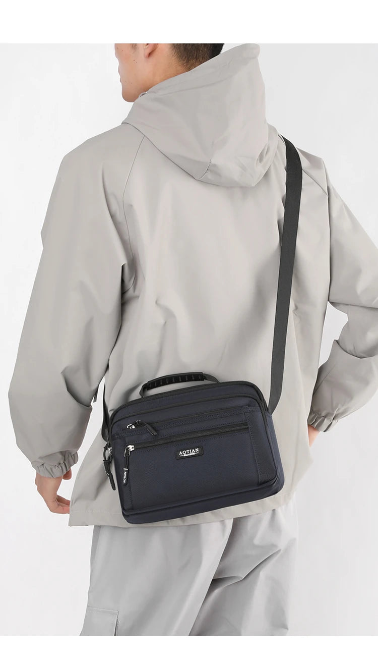 A man wearing a light gray jacket is holding a navy blue compact waterproof crossbody messenger bag.