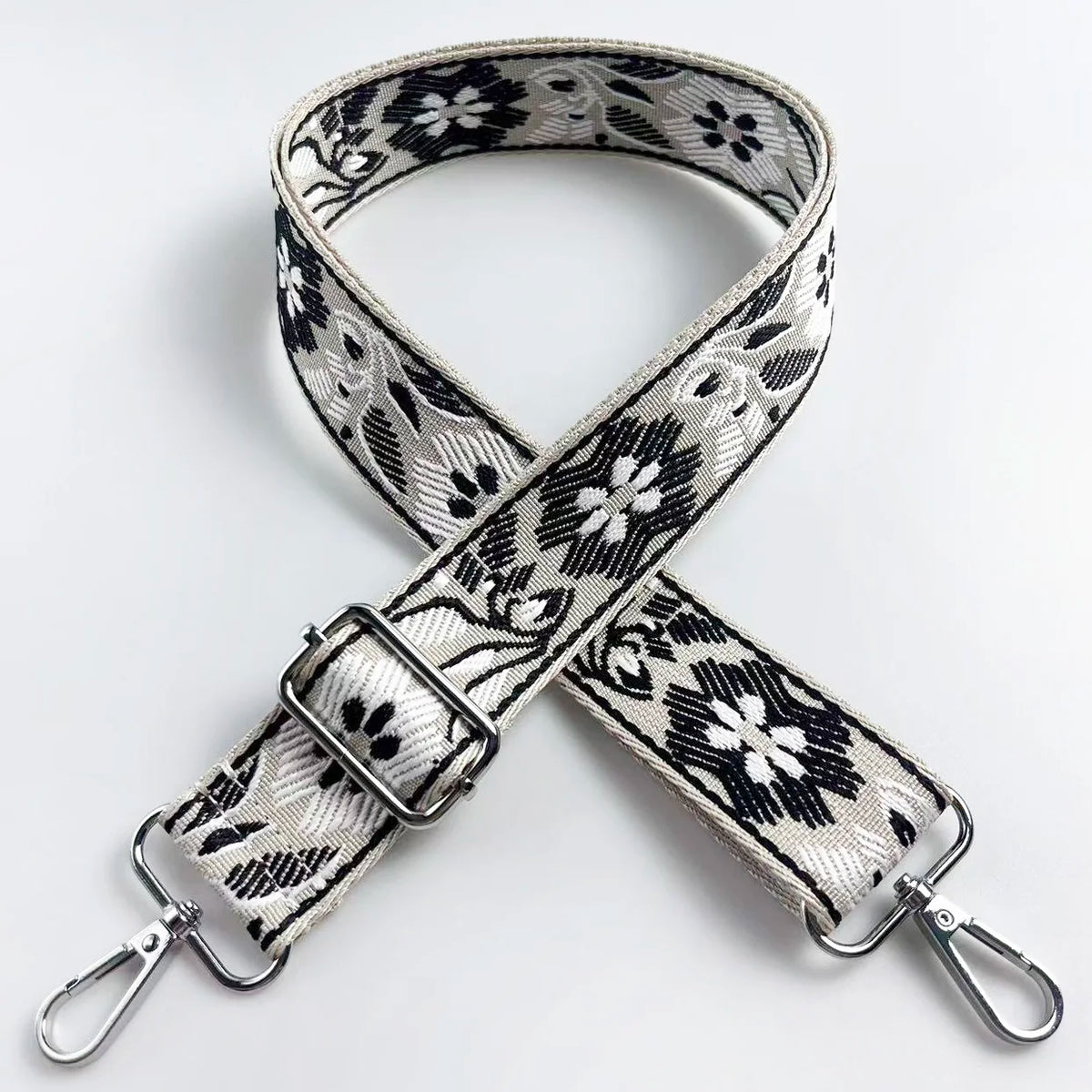 A beige and black patterned fabric strap for a crossbody bag, shown crossed.