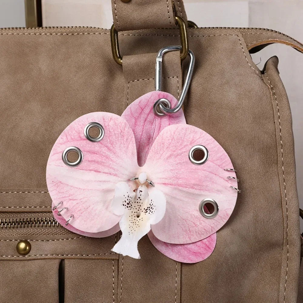 A pink orchid flower keychain attached to a brown leather handbag.