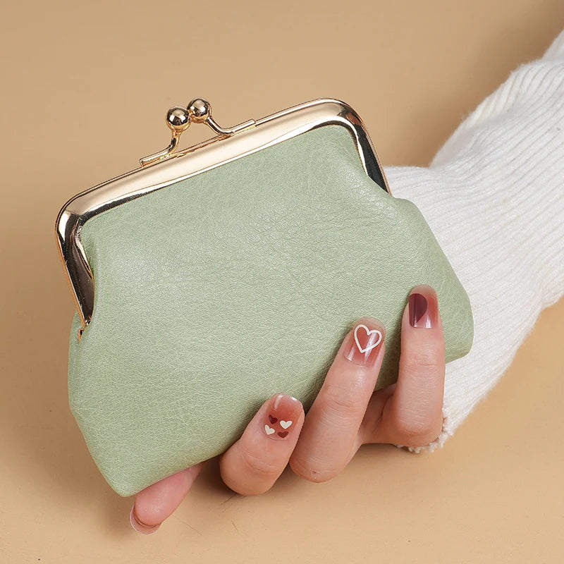 A light green coin purse with a gold buckle is held by a hand against a beige background.