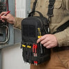 A person wearing a tan shirt holds a black tactical shoulder tool pouch filled with various tools and accessories.
