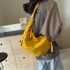 Eine Frau hält eine senffarbene Nylon-Crossbody-Tasche über einem grauen Sweatshirt.