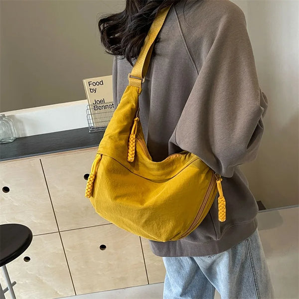 A woman is holding a mustard yellow nylon crossbody shoulder bag against a gray sweatshirt.