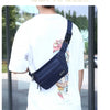 Une personne porte un petit sac imperméable bleu marine à travers sa poitrine, montré contre un t-shirt blanc.