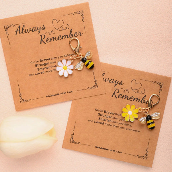 Two handmade beaded flower keychains with gold clasps and yellow and black bee charms on kraft paper cards