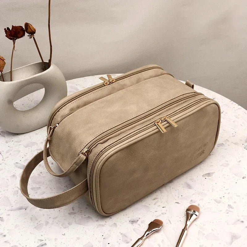 A tan PU leather travel makeup organizer bag with double zippers resting on a white marble surface.