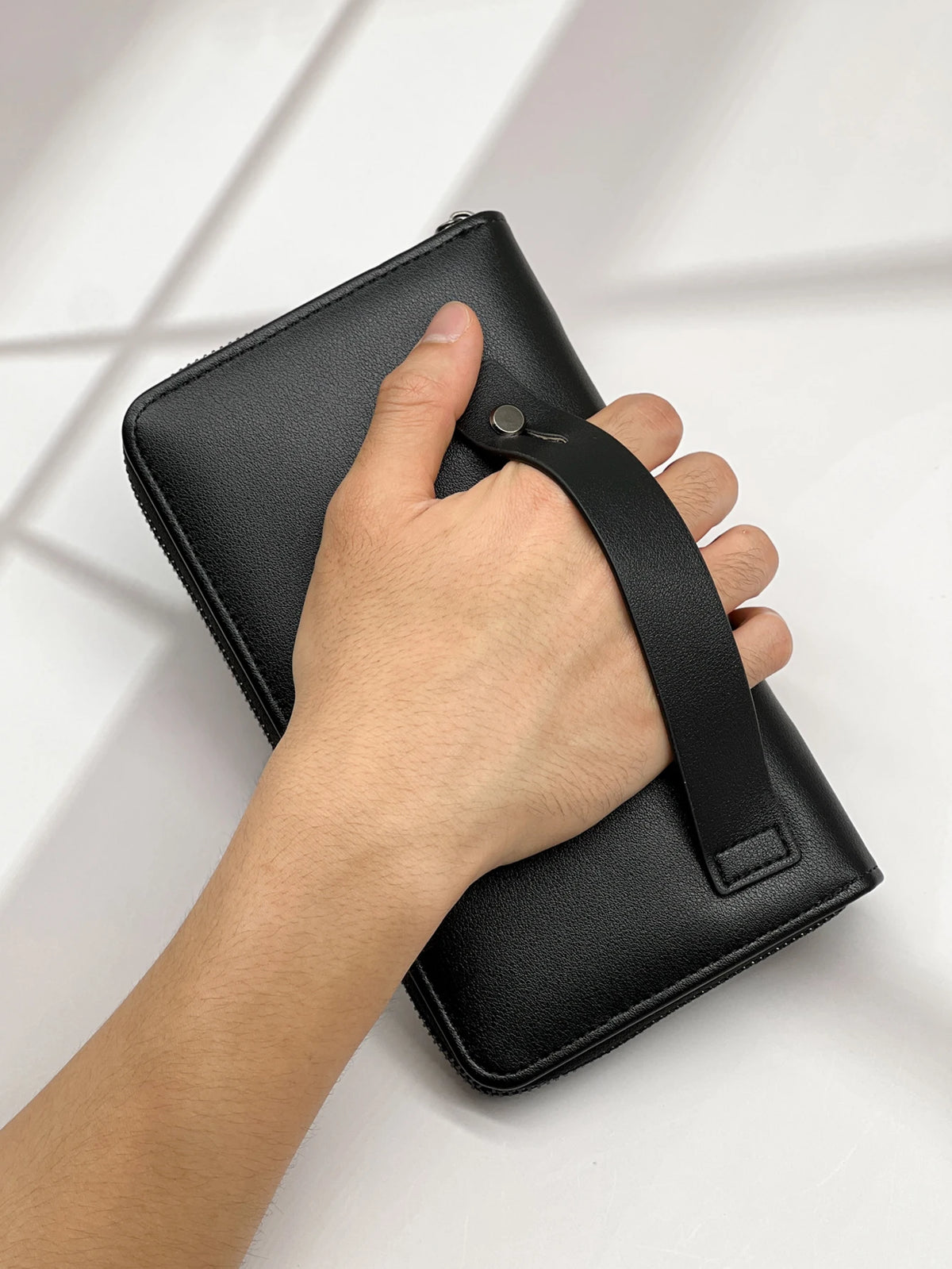 A hand holds a black multi-card men's commuter wallet with a leather strap.