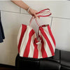 A hand holds a red and white striped canvas tote bag with a visible inner pocket.