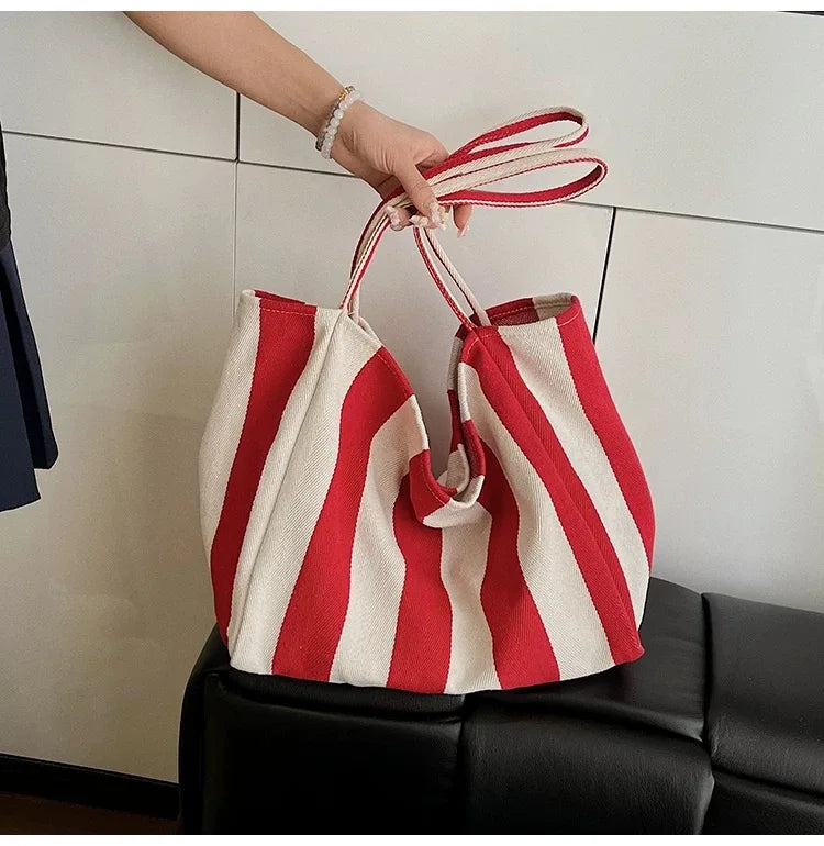 A hand holds a red and white striped canvas tote bag with a visible inner pocket.