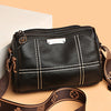 A black luxury cowhide shoulder bag with a gold hardware detail and brown leather strap is shown against a light background.