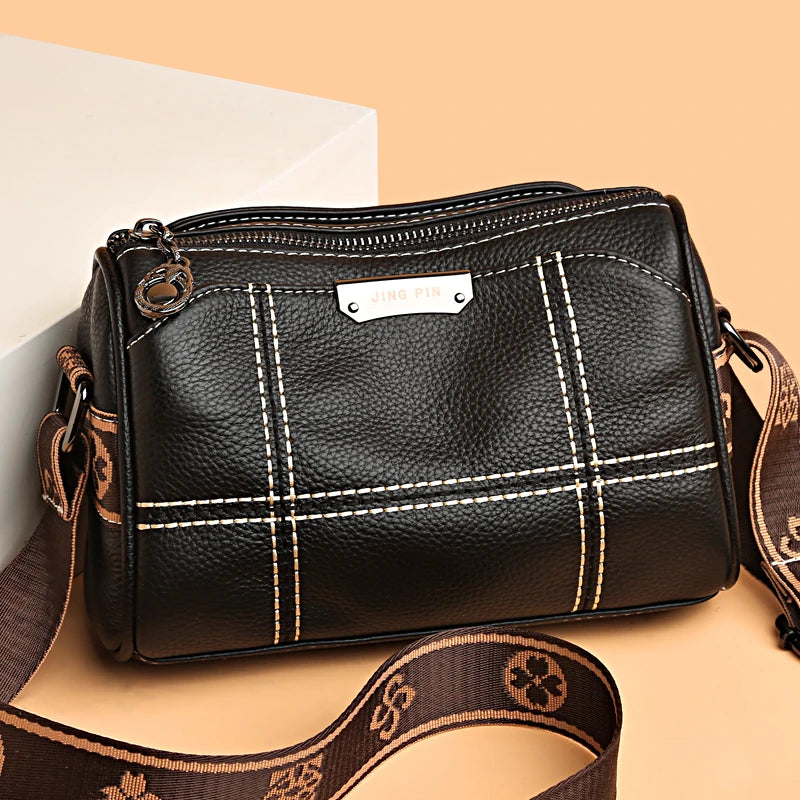 A black luxury cowhide shoulder bag with a gold hardware detail and brown leather strap is shown against a light background.