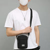 Eine Person in weißem T-Shirt und schwarzen Hosen hält eine schwarze kompakte Crossbody-Tasche.