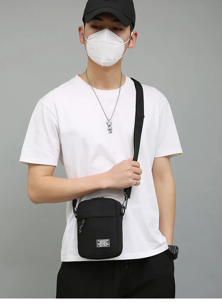 Eine Person in weißem T-Shirt und schwarzen Hosen hält eine schwarze kompakte Crossbody-Tasche.