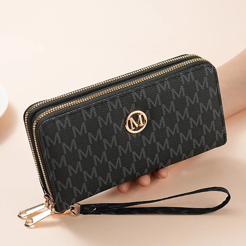 A black faux leather double zipper wallet with gold accents and a strap is shown being held by a hand.