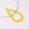 A yellow acrylic statement choker necklace with a gold-colored chain is displayed on a white plate.