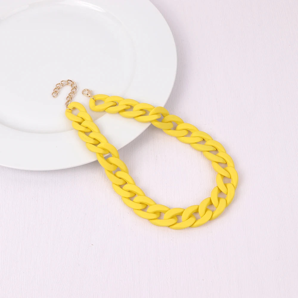 A yellow acrylic statement choker necklace with a gold-colored chain is displayed on a white plate.