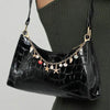 A black faux leather shoulder bag with gold chain charms and keychains worn by a person.