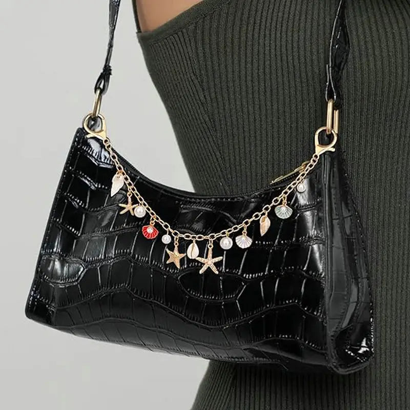 A black faux leather shoulder bag with gold chain charms and keychains worn by a person.