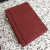 A deep red genuine leather zipper card holder and coin purse resting on a speckled surface.