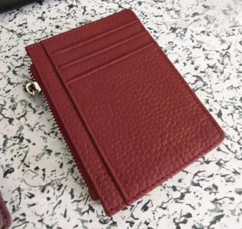 A deep red genuine leather zipper card holder and coin purse resting on a speckled surface.