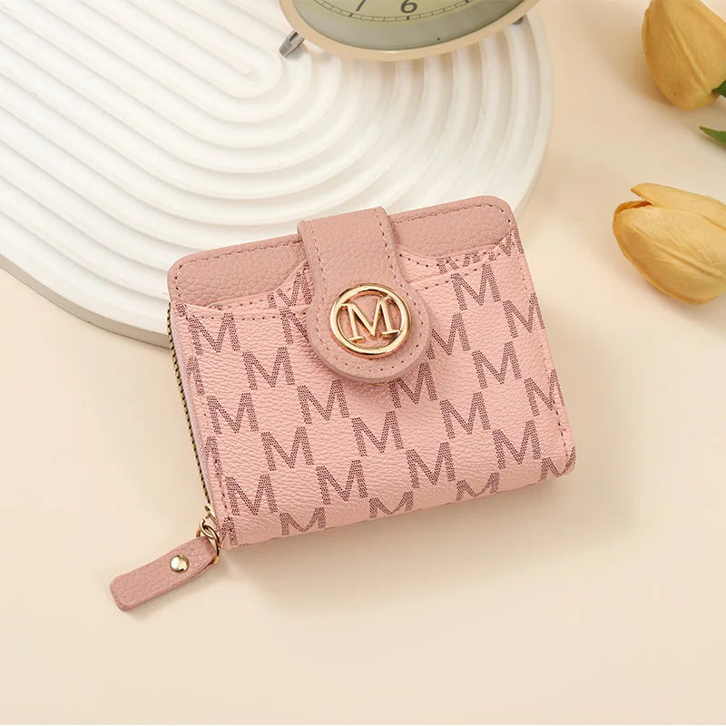 A pink vintage letter print compact wallet with a gold monogram closure resting on a light background.