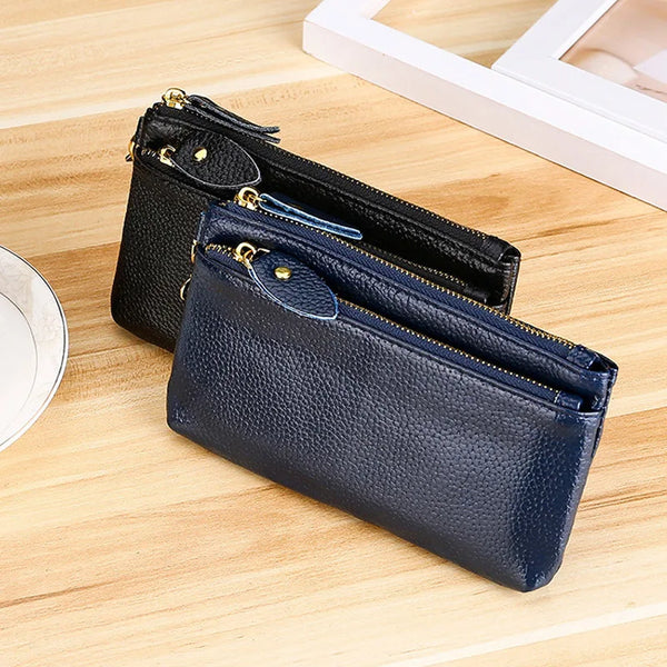 A dark blue genuine leather wristlet clutch wallet with a gold zipper closure resting on a wooden surface.