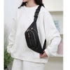A black nylon crossbody belt bag with a gold-toned strap is worn by a person in a white sweatshirt.
