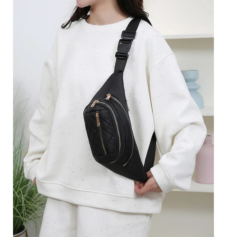 A black nylon crossbody belt bag with a gold-toned strap is worn by a person in a white sweatshirt.