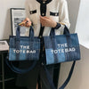 A woman holds a dark blue tote bag with white text in front of a white cardigan.