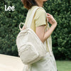 A person wearing a light yellow shirt carries a cream-colored lightweight waterproof daypack.