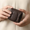 A person holds a dark brown, textured coin purse with a snap closure against a light beige fabric background.