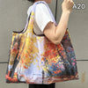 A person holds a large, colorful canvas shopping tote with an orange strap against a gray background.